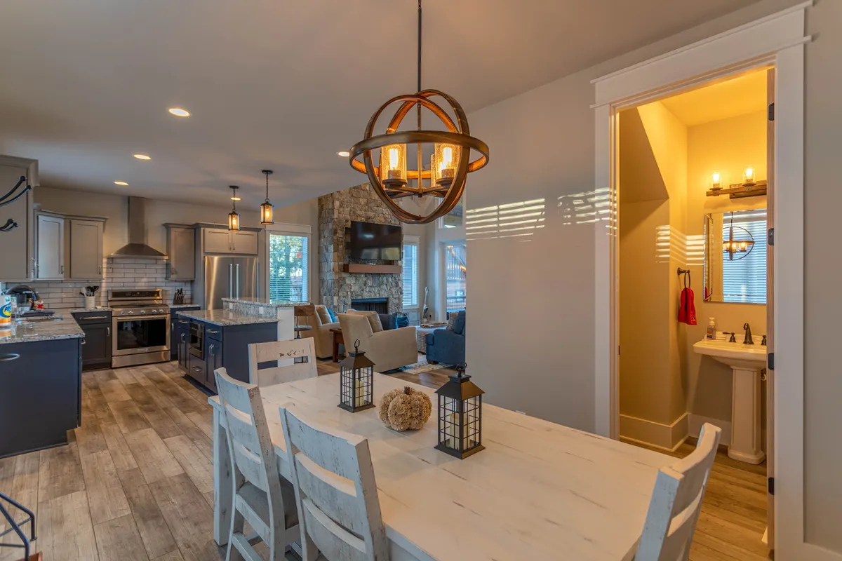 A spacious, inviting dining area with a rustic table adorned with lanterns, a modern kitchen island, a striking stone fireplace, and high-end appliances. The ambiance is warm and lively, perfect for celebrations or casual brunches.