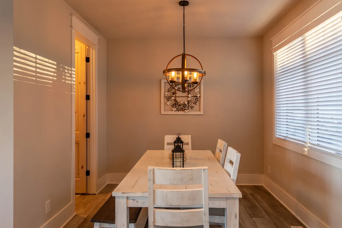A cozy dining space featuring a long wooden table set for a gathering, a dramatic chandelier overhead, elegant wall art, and a view through a wide doorway to the next room. The scene captures a moment where friends or family might gather after a day of adventure, sharing stories and meals.