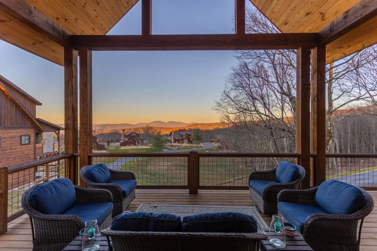 This exterior image captures a serene seating area overlooking dramatic mountain views, with warm sunlight casting a golden glow over the scene. The wooden architecture and inviting setup suggest a perfect spot for enjoying a glass of wine while reflecting or engaging in intimate conversation. The distant landscape enhances the sense of place and connection to the natural beauty of the Blue Ridge surroundings.