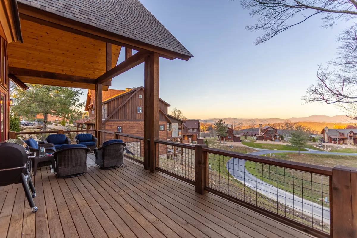 A spacious wooden deck with comfortable seating overlooks sweeping mountain views. The arrangement invites relaxation or social gatherings, while the vantage point emphasizes unobstructed panoramas and the immersion in nature. The scene is lit with soft, natural light, hinting at both sunrise and sunset appeal.
