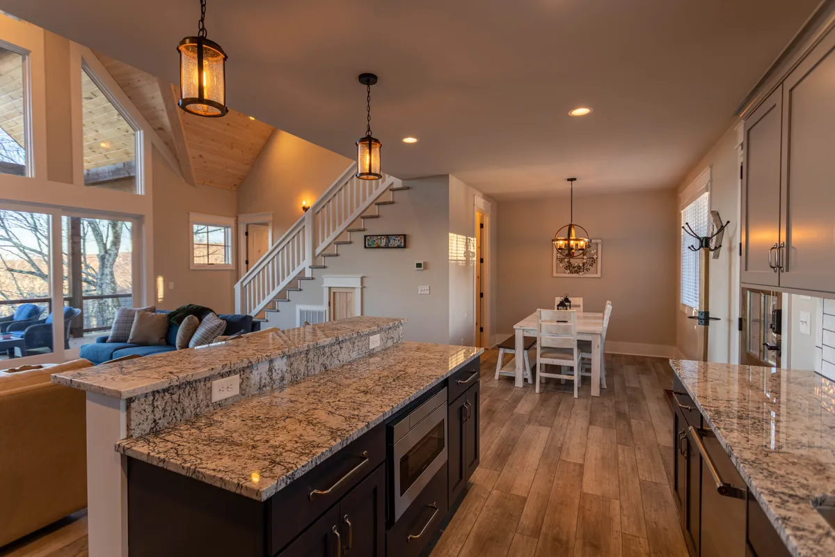 A thoughtfully arranged interior featuring a granite kitchen island, an 8-seat dining table, elegant lighting fixtures, and large windows framing mountain vistas. The open layout encourages both meal preparation and group dining in a sunlit, sociable setting.