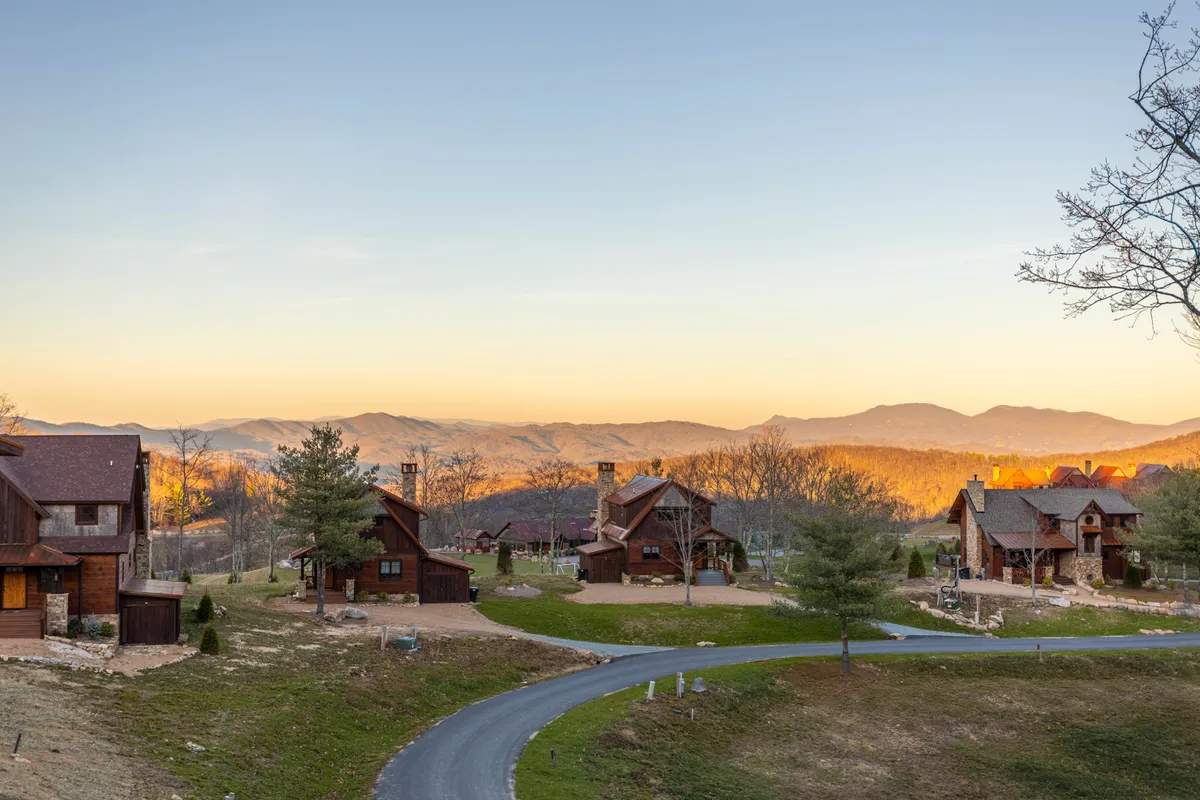 A sweeping view of the mountain range with rustic wooden cabins and a winding road in the foreground. The golden-hour lighting accentuates the natural landscape, inviting guests to explore hiking trails, soak in the fresh air, and take in the stunning vistas that define the area surrounding Eagles Nest Winery.