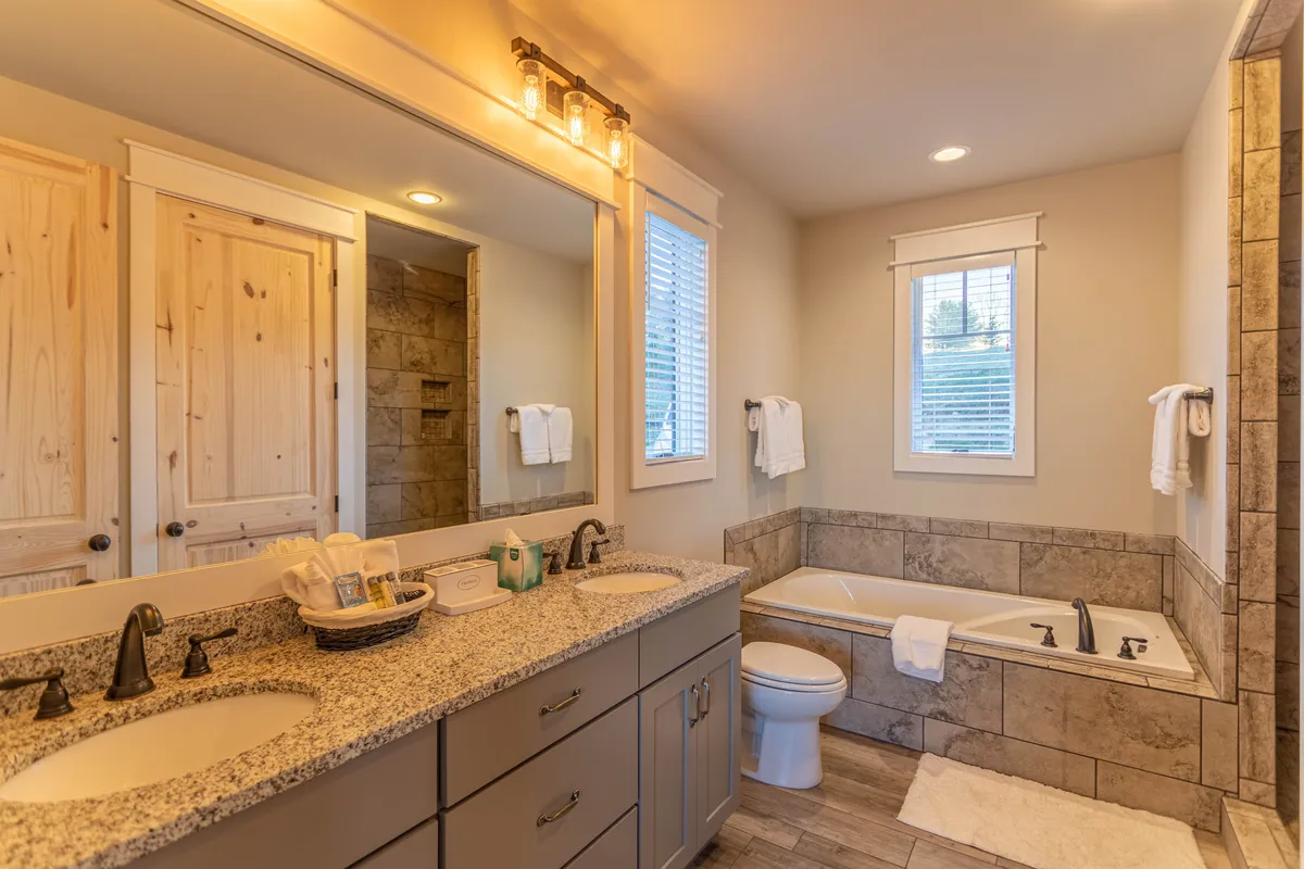 A spa-like bathroom with a double sink vanity, a luxurious bathtub, a mirrored wall, and modern light fixtures. The space feels bright and serene, inviting guests to indulge in pampering routines or enjoy a relaxing soak.
