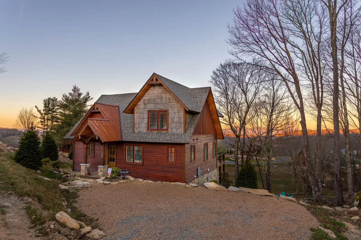 The home nestled among trees at sunset, with a porch that invites relaxation and a peaceful transition between indoors and the surrounding wilderness. The setting is tranquil, suggesting morning coffee outside, stargazing, and easy access to nature.